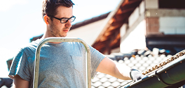 A gentleman wearing glasses cleaning his gutters