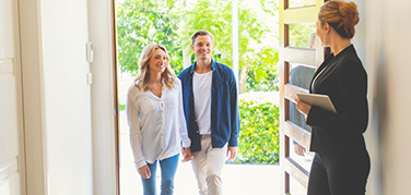 A man and woman walking into a house being met by a lady realtor